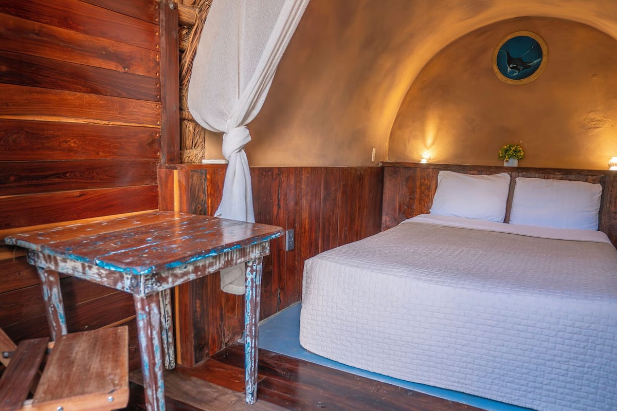 A rustic room with a wooden bed, a small table, and a hanging light fixture.
