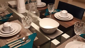 A dining table set with white plates, bowls, and cutlery, with a clear glass vase and a white pitcher. - Apartamento da Cor do Mar - VR-1202 (Recife)