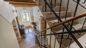 A staircase with a wooden handrail and black metal balusters, leading to a room with a stone wall, a window, and a sewing machine on a table. - CASA SAINA - Studio Limone (Rovinj)