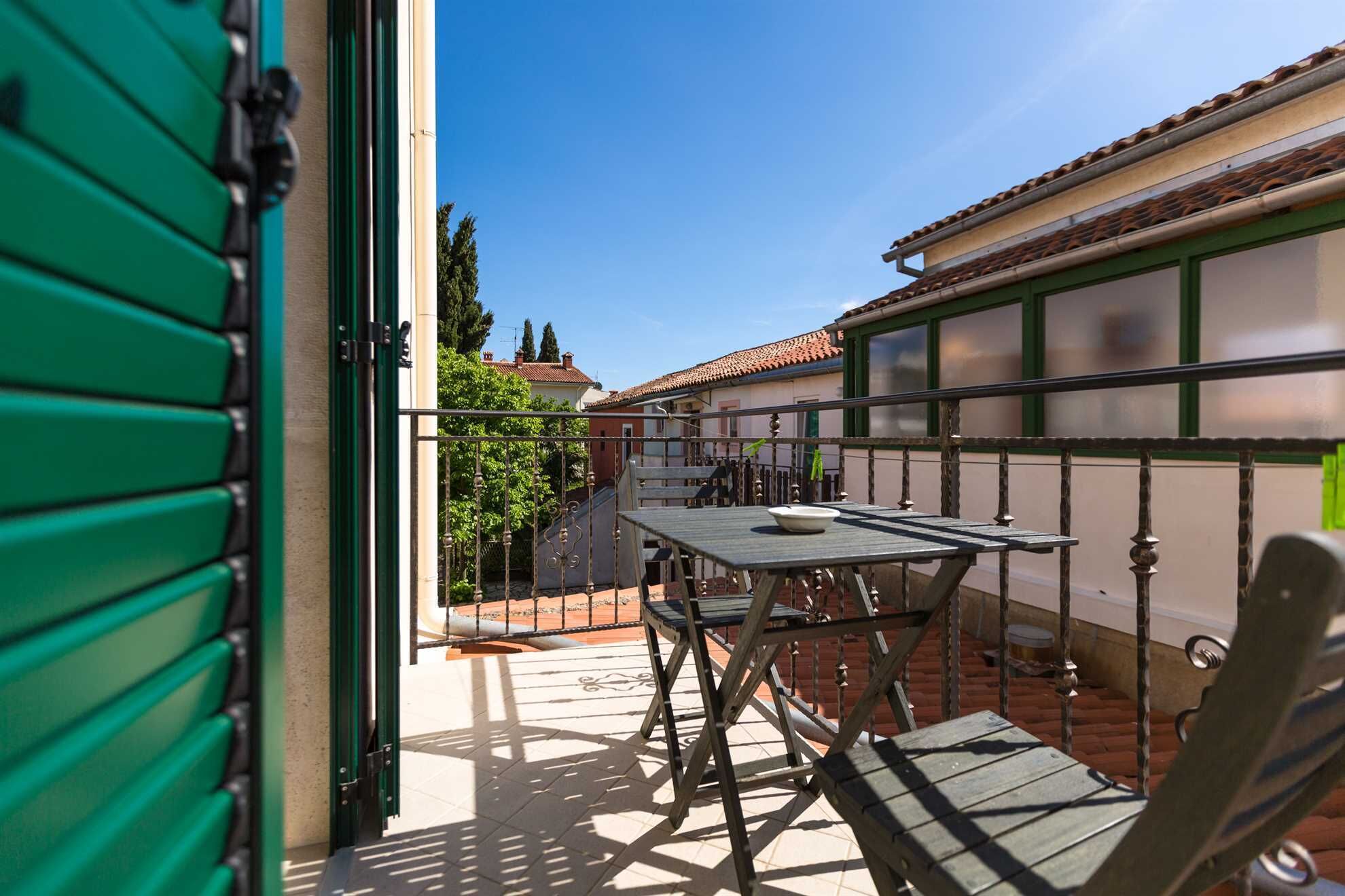 Un balcon avec une table et des chaises, une rambarde en métal et une vue sur un quartier résidentiel avec des maisons et des arbres.