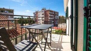 Un balcón con mesa y sillas, con vistas a una zona residencial de techos de teja y un edificio de varios pisos.