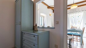 Una habitación con un armario azul, una mesita con sillas, y un comedor visible a través de una puerta abierta.