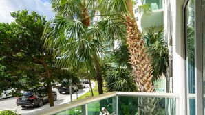 A balcony with white metal chairs and a small table, overlooking a street with cars and palm trees. - 
Miami CONDO Family-Friendly Beach Condo w/ Full Kitchen, Aventura Mall (Sunny Isles)