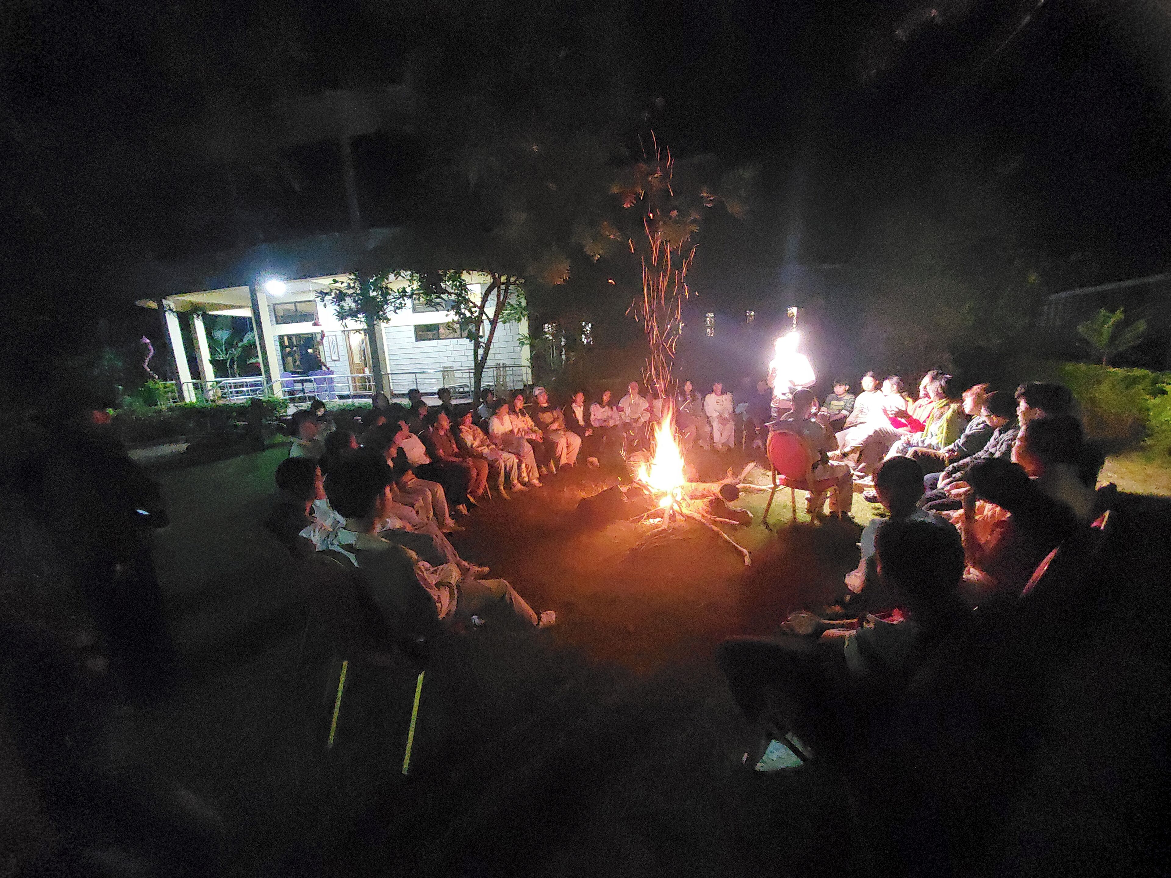 A group of people seated around a campfire at night.