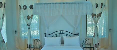 Una habitación con una cama, dos sillas y un ventanal con cortinas.