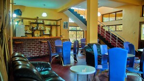 A restaurant with a brick wall, blue chairs, a leather couch, and a staircase. - Ngorongoro Corridor Lodge (Karatu)