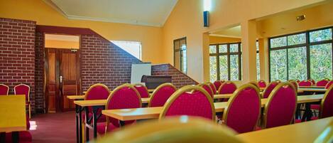 A dining area with brick walls, wooden tables, and red chairs.
