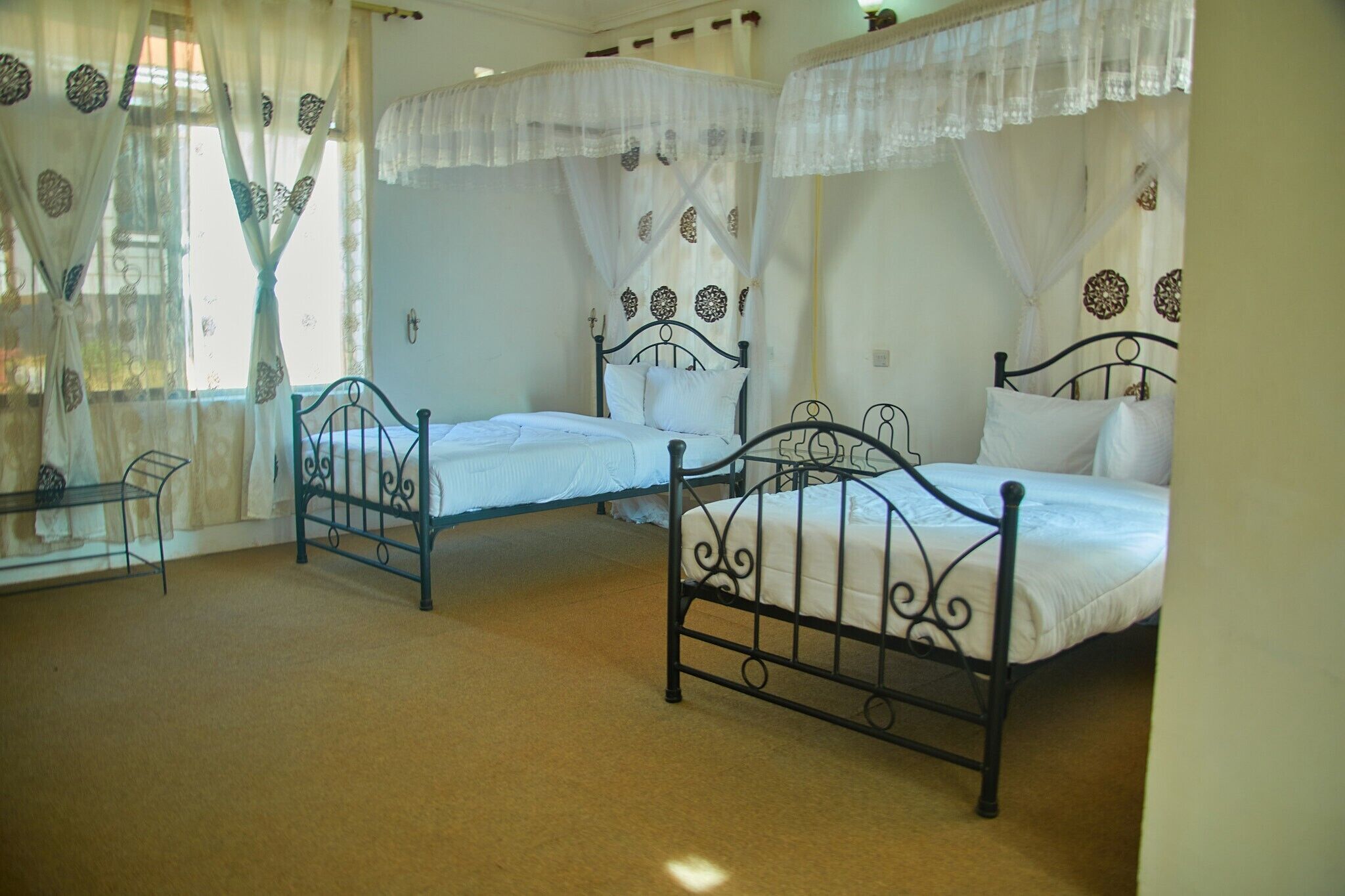 A room with three beds, each with a canopy. There is a small table and a window with curtains.