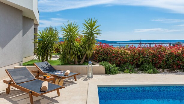 A poolside area with lounge chairs, a small table with a drink, and a view of the sea.