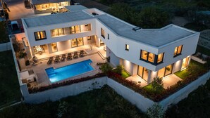 A modern two-story house with a swimming pool, outdoor seating, and a well-lit patio area.