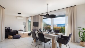A modern dining area with a large table, chairs, and a view of the outdoors.