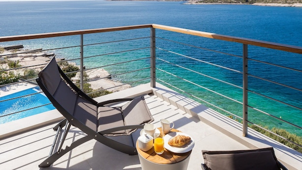 En balkong med utsikt över havet, en pool och ett bord med frukostmat.