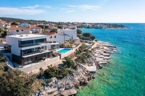 Una propiedad costera con un edificio moderno de dos pisos, piscina privada y costa rocosa.