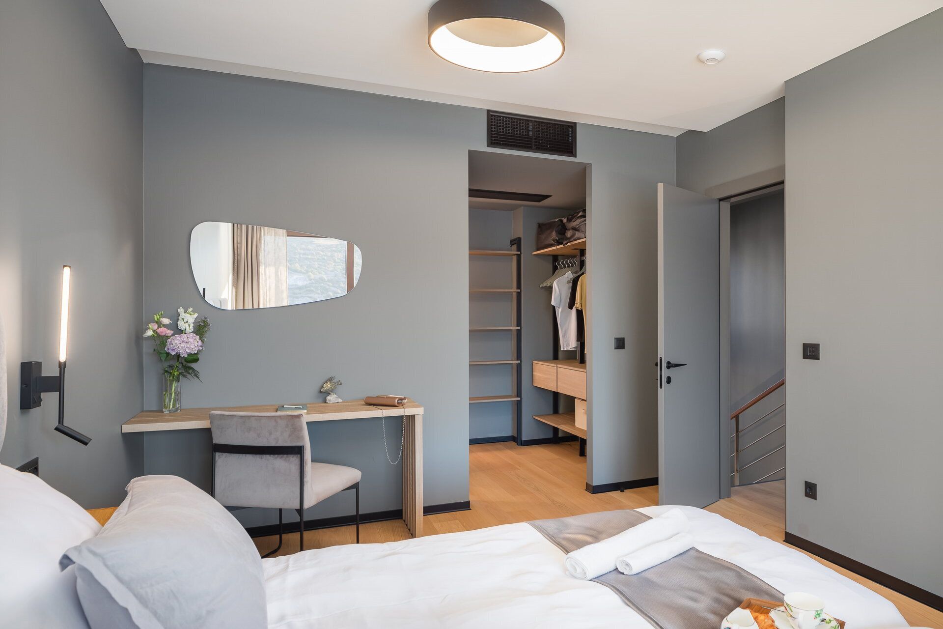Una habitación de hotel moderna con cama, escritorio, silla, espejo, armario y baño.