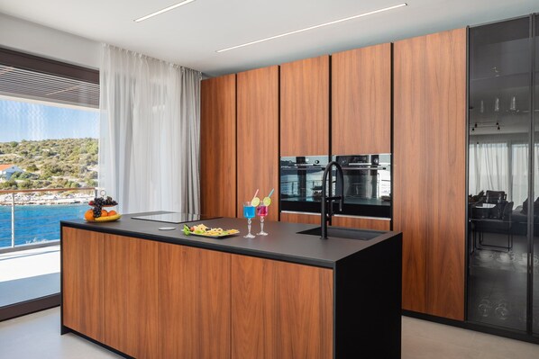 A modern kitchen with wooden cabinets, a black countertop, and a view of the sea.