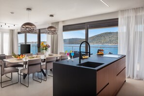 A modern kitchen with a large island, dining area, and a view of the sea.