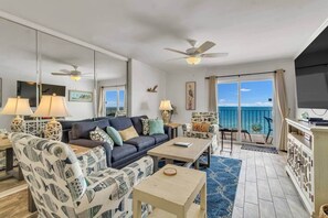 A living room with a sofa, armchairs, a coffee table, a TV, and a balcony with a view of the sea.