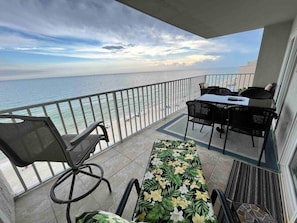 A balcony with a view of the sea, a table, chairs, and a small garden area.