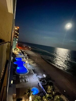 A beachfront hotel with a pool area, a view of the ocean, and a building with illuminated windows.