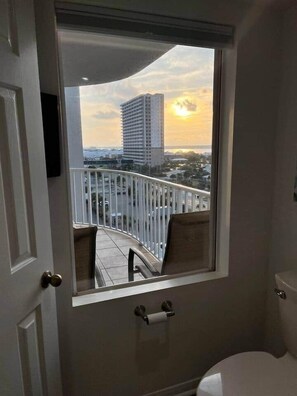 A bathroom with a toilet, a window, and a view of a balcony with a railing.