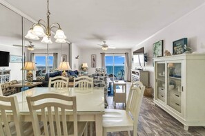 A spacious living area with a dining table, chairs, a ceiling fan, and a view of the sea.