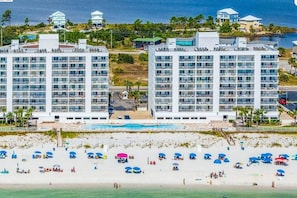 A beachfront hotel with multiple high-rise buildings, a swimming pool, and beach umbrellas.