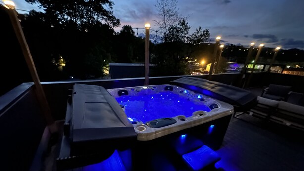 Un bain à remous doté d’un éclairage LED bleu, installé sur une terrasse en bois et entouré de mobilier d’extérieur.