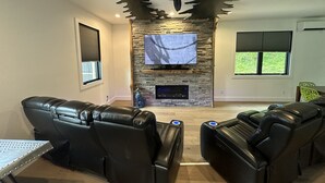 Un salon moderne avec une cheminée en pierre, un téléviseur fixé au mur et des fauteuils en cuir inclinables.