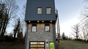 Une maison moderne à deux étages, dotée d’une façade en pierre, d’un garage et d’une porte verte.