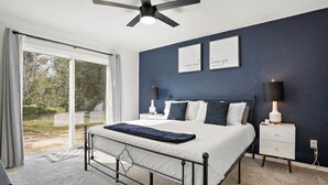A bedroom with a bed, bedside tables, a ceiling fan, and a view through a glass door. - Beautiful summer open concept house that feels like home away from home, exceptionally clean with a great outdoor space and fire pit! Near speedway, airport, and beach! (Port Orange)