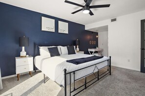 Une chambre à coucher avec un lit, des tables de chevet, un ventilateur de plafond et des œuvres d’art encadrées accrochées au mur.