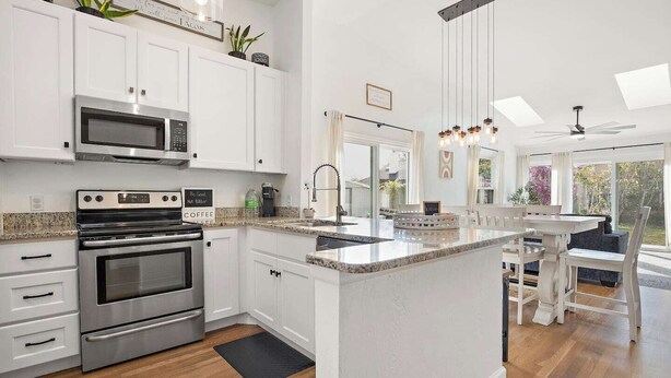 A modern kitchen with white cabinetry, a built-in oven, a coffee station, and a breakfast bar with seating. - Beautiful summer open concept house that feels like home away from home, exceptionally clean with a great outdoor space and fire pit! Near speedway, airport, and beach! (Port Orange)