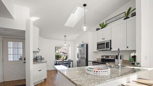 A modern kitchen with white cabinetry, a granite countertop, and stainless steel appliances. - Beautiful summer open concept house that feels like home away from home, exceptionally clean with a great outdoor space and fire pit! Near speedway, airport, and beach! (Port Orange)