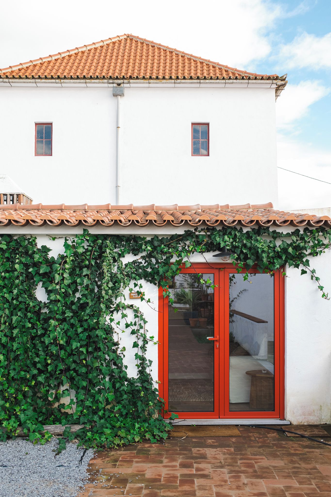 A building with a tiled roof, a red door, and a wall covered in green ivy.