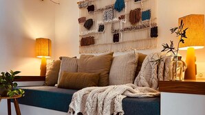 A cozy living room with a sofa, cushions, a macrame wall hanging, and two lamps.