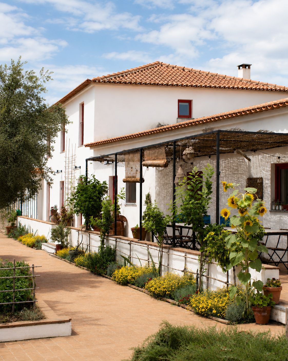 A white building with a tiled roof, a covered patio area, and a variety of potted plants and flowers.