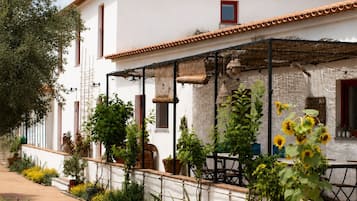 A white building with a tiled roof, a covered patio area, and a variety of potted plants and flowers.