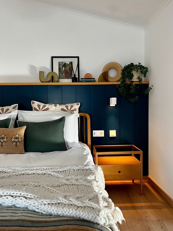 Une chambre à coucher comprenant un lit, une table de chevet, une étagère murale décorée de divers objets et une plante en pot.