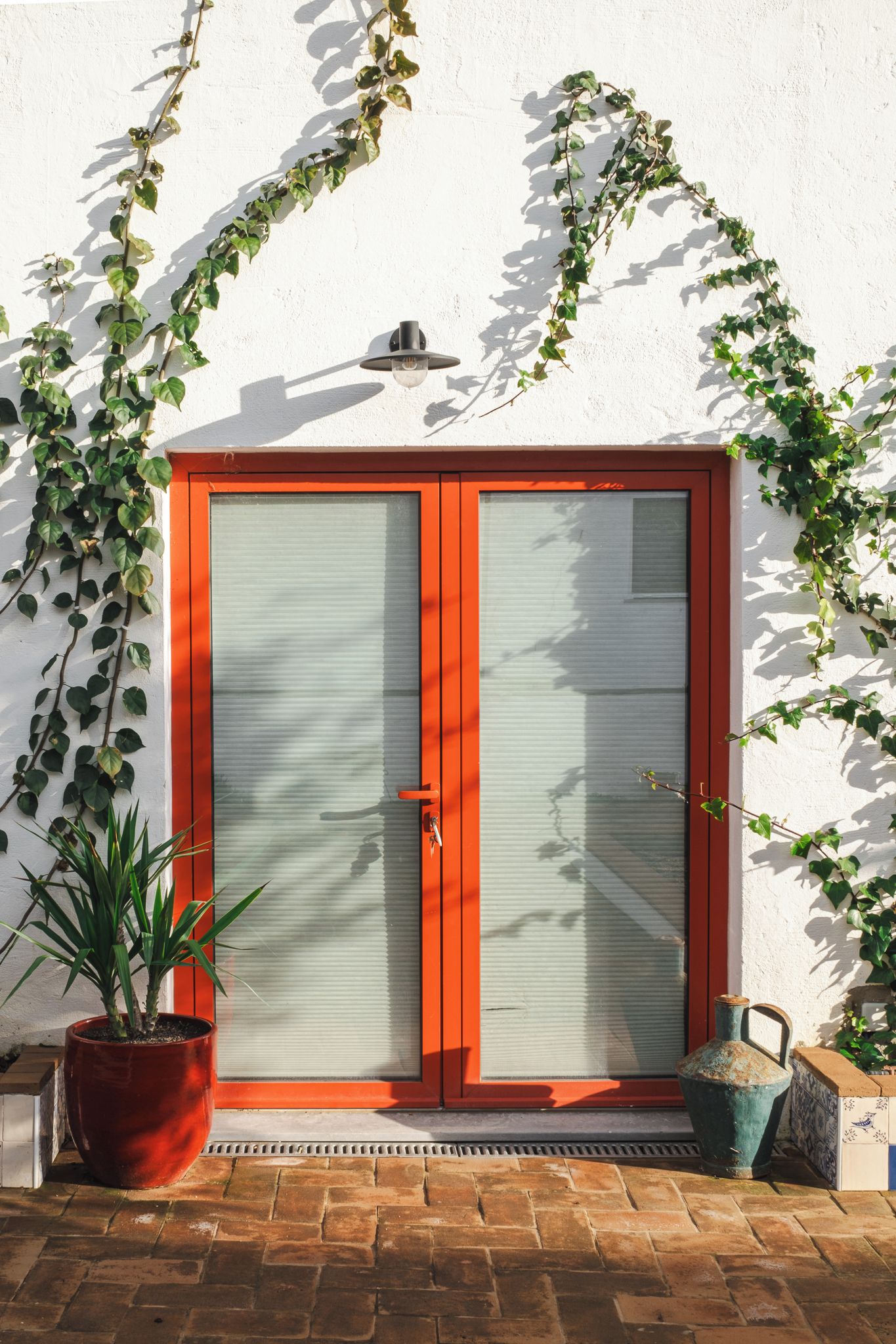 Una puerta con marco rojo, una ventana, una planta en maceta y un aplique de pared.