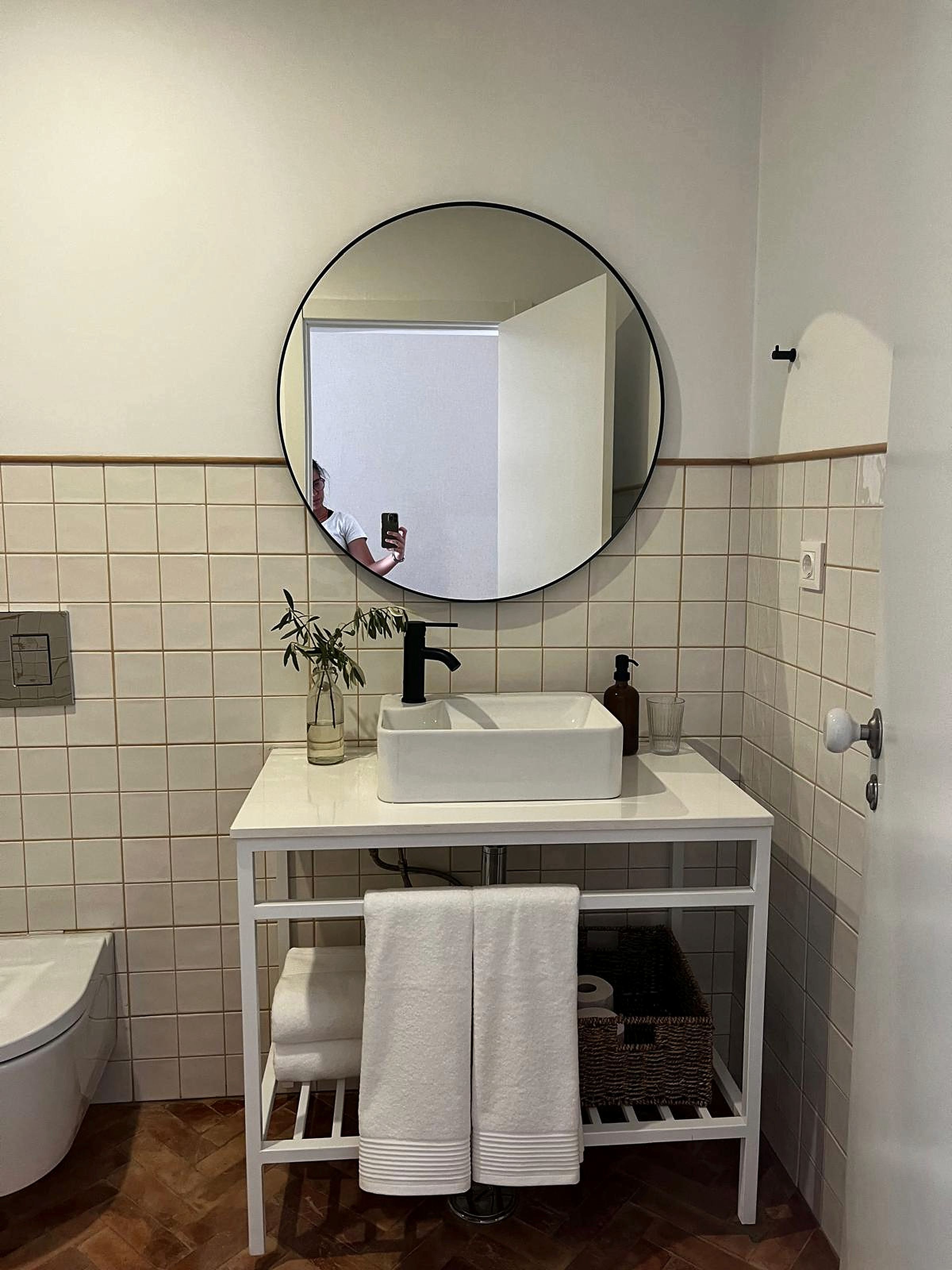 Un baño con un lavamanos blanco, un espejo redondo y un inodoro blanco.