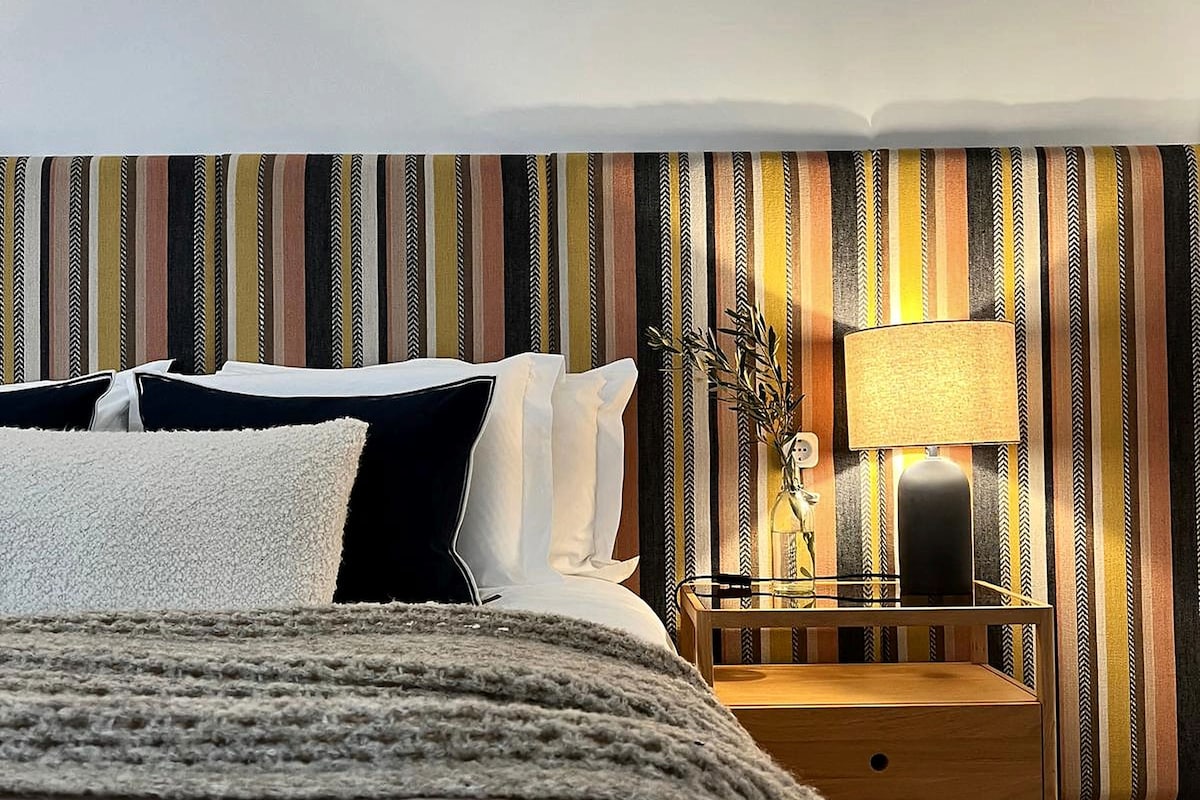 A bedroom with a bed, bedside table, lamp, and a striped wall.