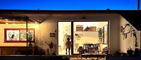A house with a dining area, a kitchen visible through a window, and a person walking towards the entrance.