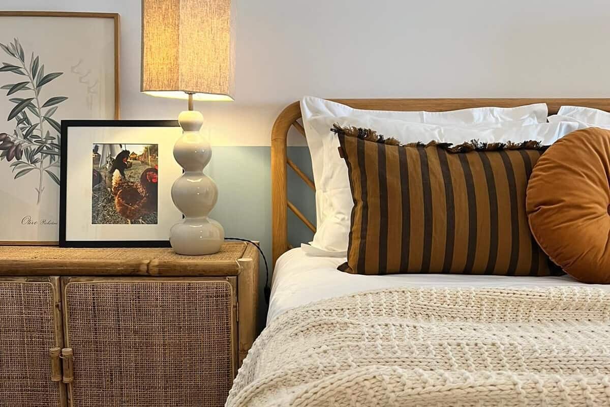A neatly made bed with a patterned blanket, a bedside lamp, and a framed picture on a nightstand.