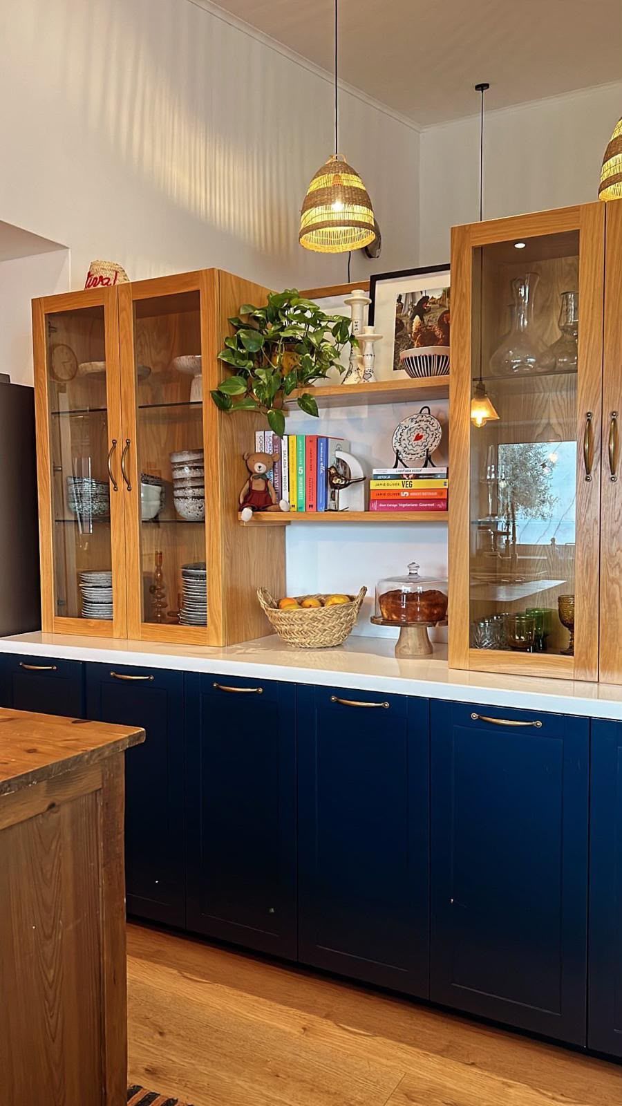 A kitchen with wooden cabinets, a central island with a basket of fruit, and hanging pendant lights.