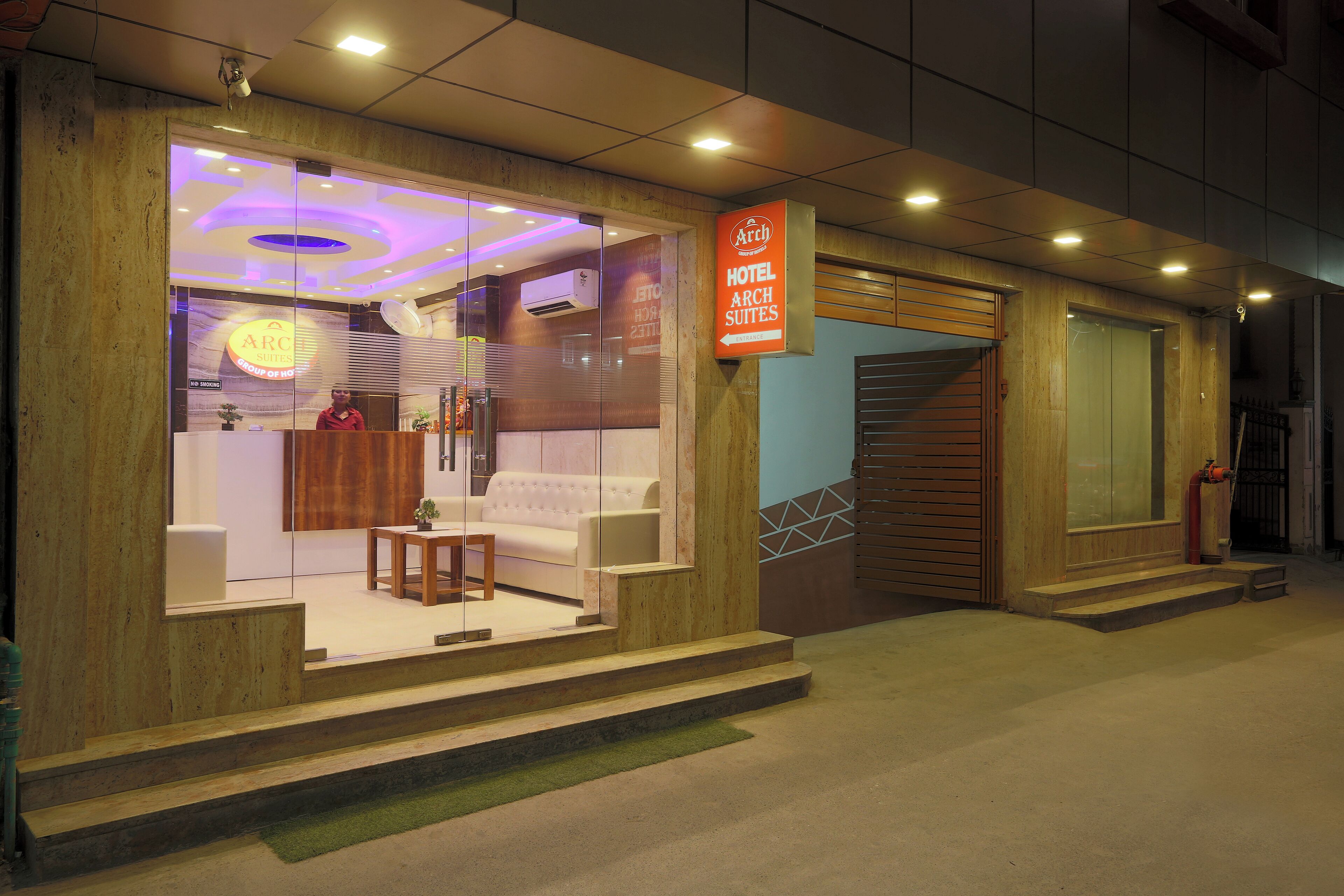 A hotel entrance with a reception desk, a staircase, and a sign indicating 'Hotel Arch Suites'.