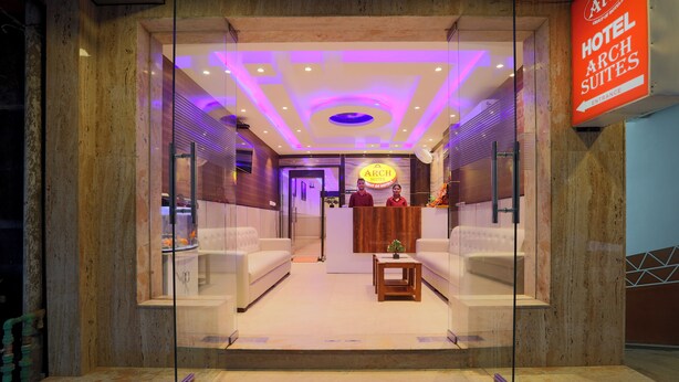 A hotel lobby with a reception desk, two sofas, a small table, and a sign indicating the hotel name and suites. - Hotel Arch Suites (New Delhi)