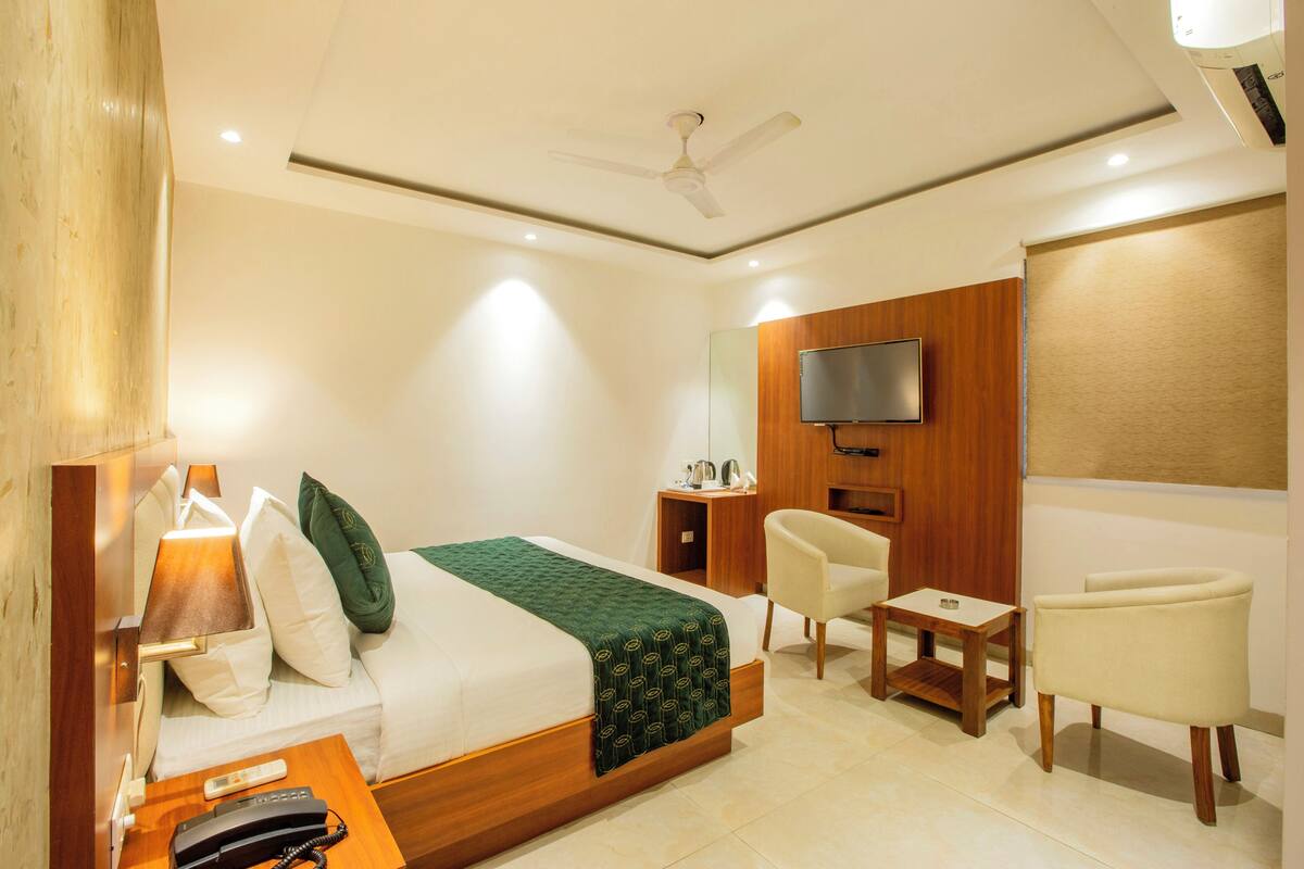 A hotel room with a bed, bedside table, chair, TV, and a small table.