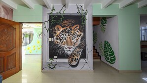 A hallway with a large painting of a leopard's face, a wooden door, and a staircase with green leaf decorations. - Macondo Hostel (Santa Marta)