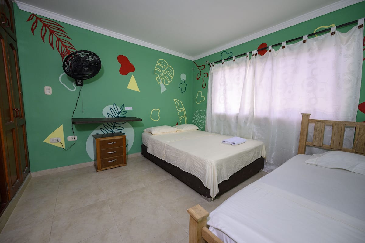 A bedroom with two beds, a fan, and a dresser.