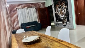 A dining area with a wooden table, white chairs, a blue sofa, and a wall mural of a leopard. - Macondo Hostel (Santa Marta)